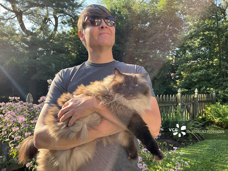 男人在花园里抱着他的布偶猫图片素材