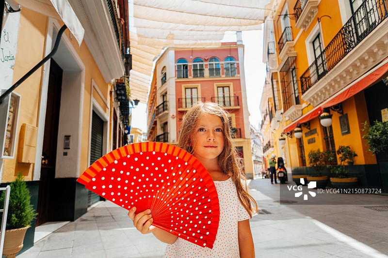 美丽女孩手持红扇在西班牙塞维利亚都市阳伞前摆姿势图片素材