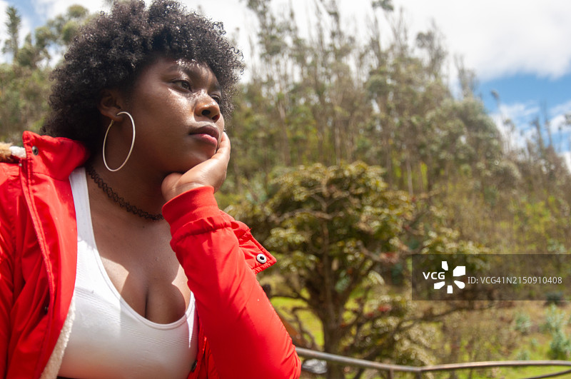 一位沉思的非洲裔年轻女人在户外，周围环绕着绿色植物，在阳光明媚的日子里为未来做决定图片素材