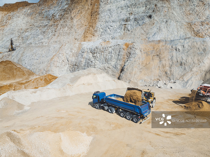 挖掘机向蓝色自卸卡车装载砂砾的航拍照片图片素材