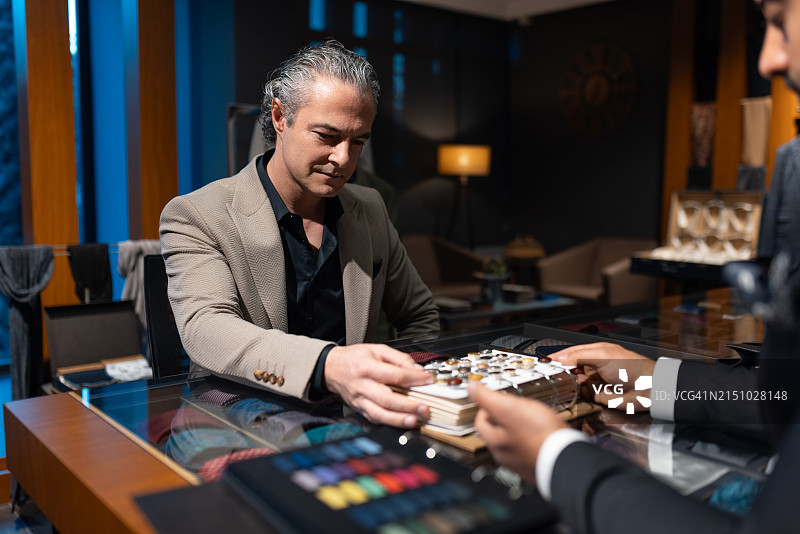 穿着西装的自信商人正在私人裁缝处挑选新西装的面料和纽扣图片素材