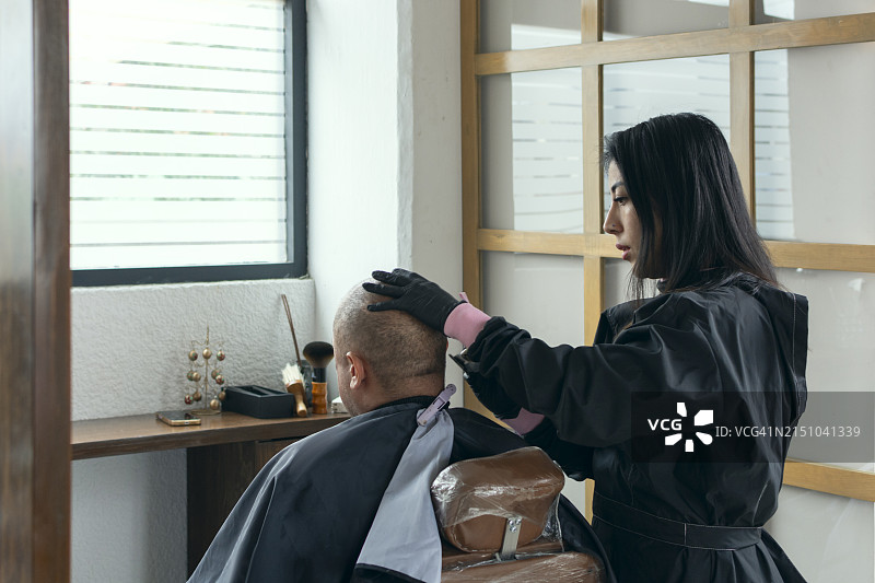 女人为一名男子剃头，为他治疗脱发图片素材