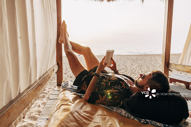 男人在海滩度假小屋里躺着看书图片素材
