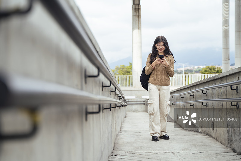年轻女子在使用智能手机时穿过混凝土桥图片素材