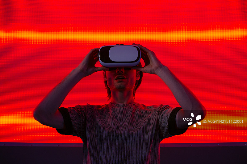 惊讶的年轻男子在霓虹灯墙背景上佩戴VR眼镜图片素材