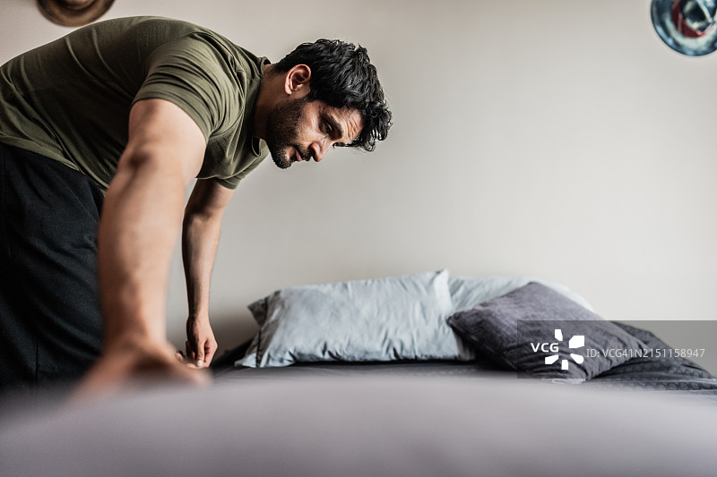 中年男人在家里的卧室里整理床铺图片素材