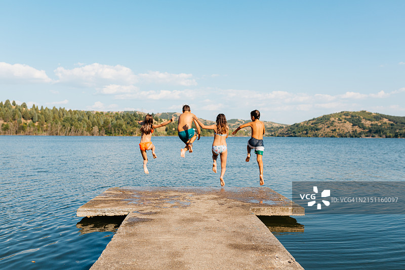 孩子们在炎热的夏日里从码头跳入湖中玩耍图片素材