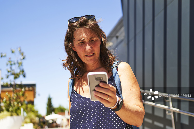 身穿休闲服和太阳镜站在街上用手机打字的漂亮女人肖像，正面视角图片素材