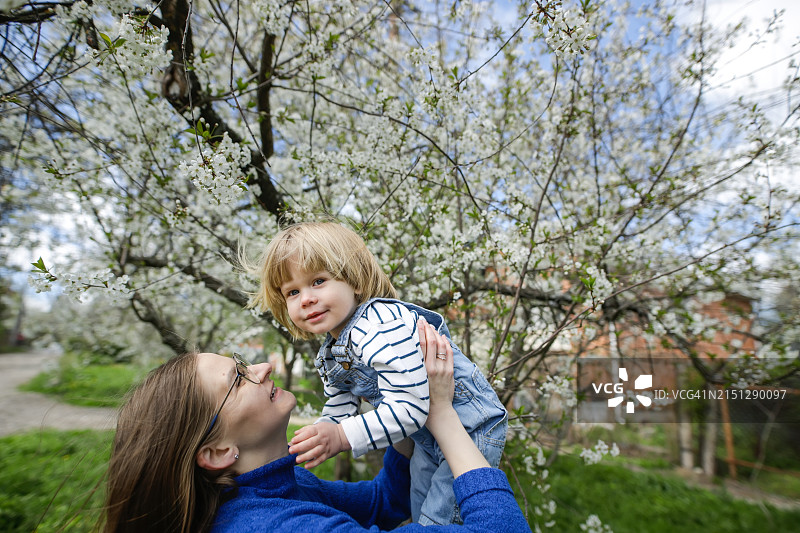 春日温馨：中年母亲与幼儿在盛开的树木中嬉戏图片素材