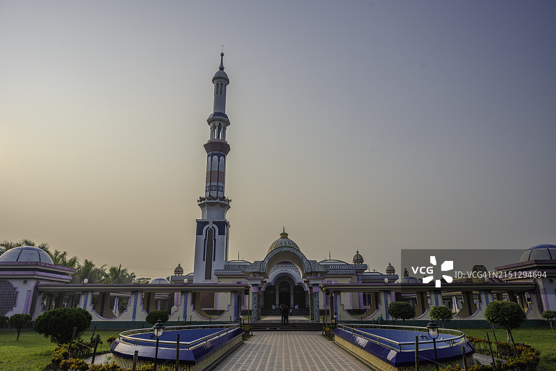 孟加拉国巴里萨尔的巴伊图尔阿曼贾米清真寺，在午后阳光下，拥有宣礼塔、装饰穹顶、反射水景和维护良好的花园图片素材