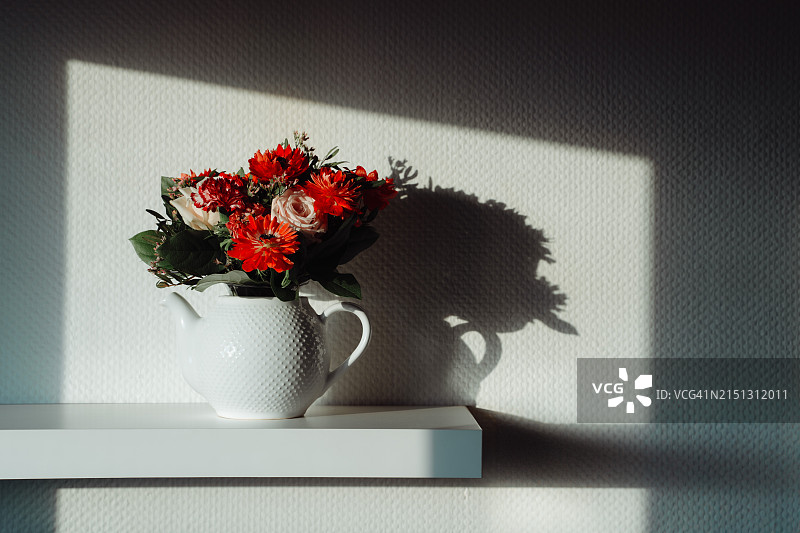 阳光明媚的日子里，陶瓷茶壶中的红色花朵图片素材