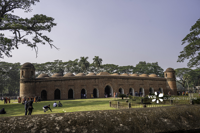 阳光下，游客们挤满了巴盖尔哈特六十圆顶清真寺的庭院，古老的砖块和参天大树为这个联合国教科文组织遗址遮荫。图片素材