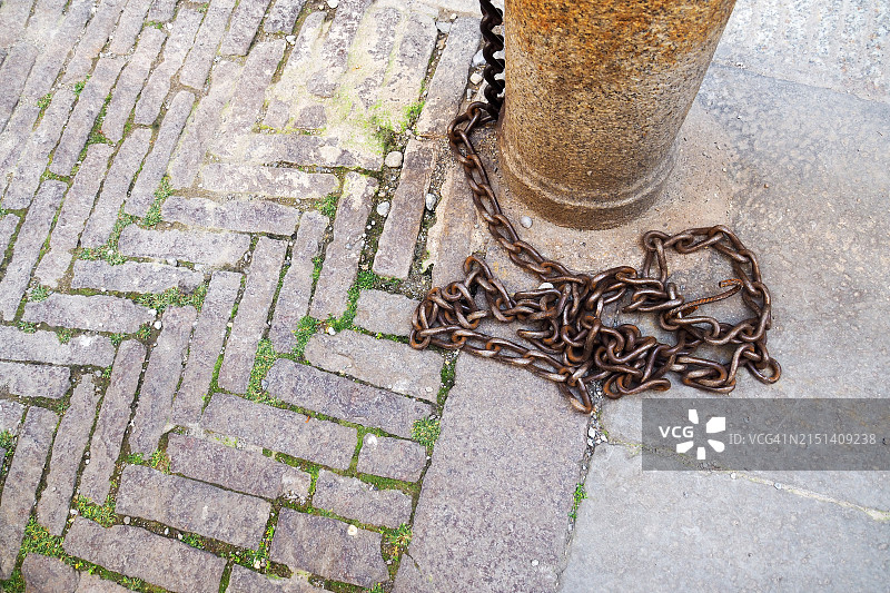石板路面上带有生锈链条的古老柱子图片素材