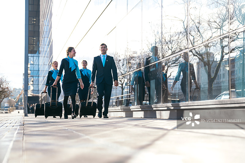 微笑的航空公司机组人员拉着行李在机场行走图片素材