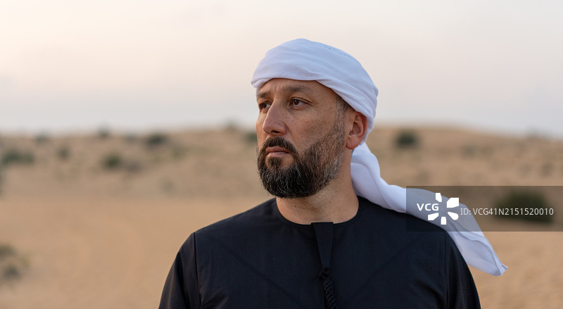 身穿阿拉伯传统服装在迪拜沙漠中摆姿势拍照的男人图片素材