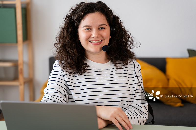 戴耳机在家用笔记本电脑工作的微笑女子图片素材
