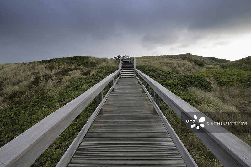 傍晚穿过沙丘的木板路；欧洲，德国，石勒苏益格荷尔斯泰因州，叙尔特岛，北弗里西亚群岛，坎彭，北海图片素材