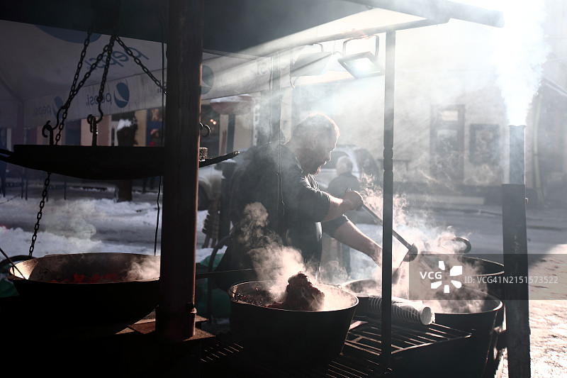 男人在食品摊位上供应热气腾腾的炖菜图片素材