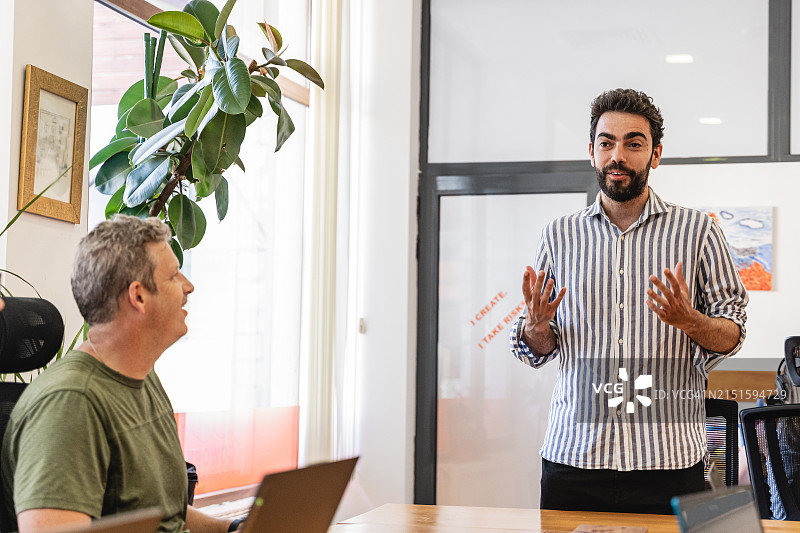 年轻的男商人在办公室里和同事交谈图片素材