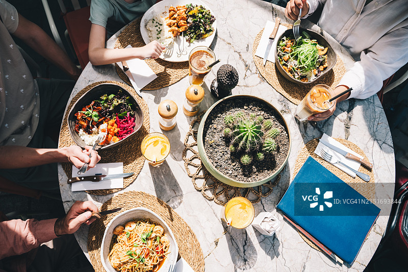 一群朋友坐在咖啡馆里吃各种菜肴，阳光明媚的一天从上方俯视。无法辨认的人。图片素材