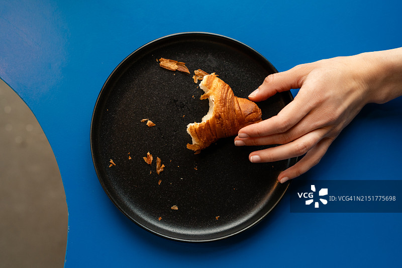 手拿盘中吃了一半羊角面包的俯视图图片素材