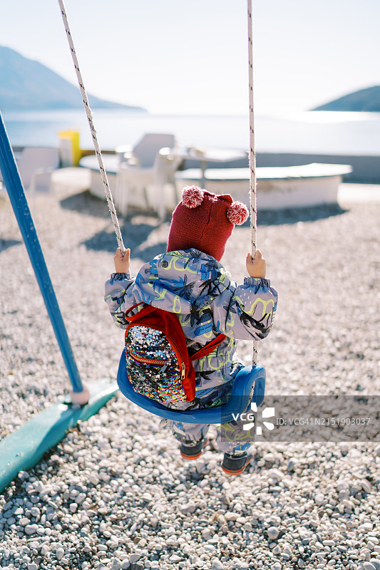 阳光明媚的日子里，背着背包、穿着工作服的儿童在荡秋千图片素材