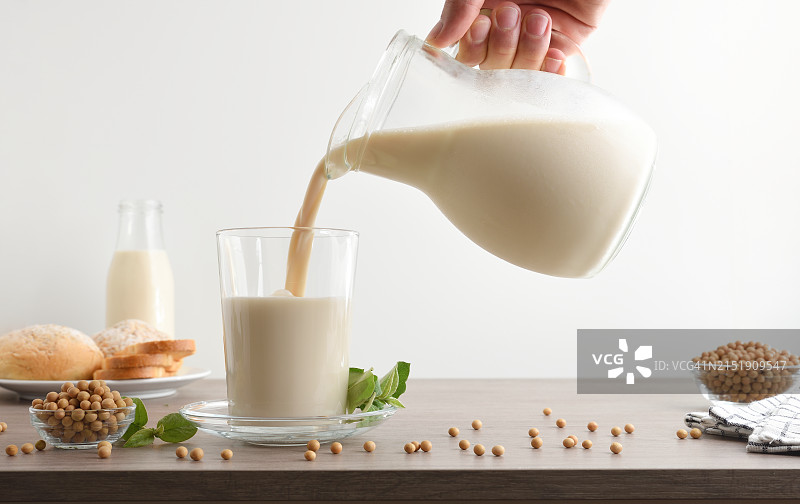 从水壶中将豆浆倒入玻璃杯中，白色隔离图片素材