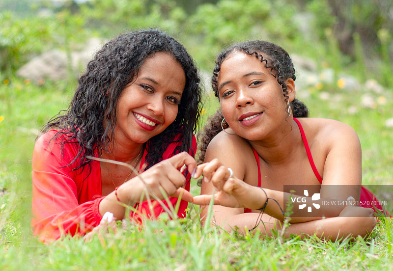 两个拉丁裔朋友俯卧着，对着镜头微笑，用手比心图片素材