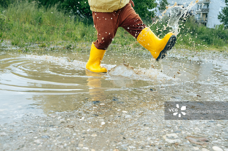 儿童户外无电子设备娱乐：穿着黄色雨靴的孩子走过水坑图片素材