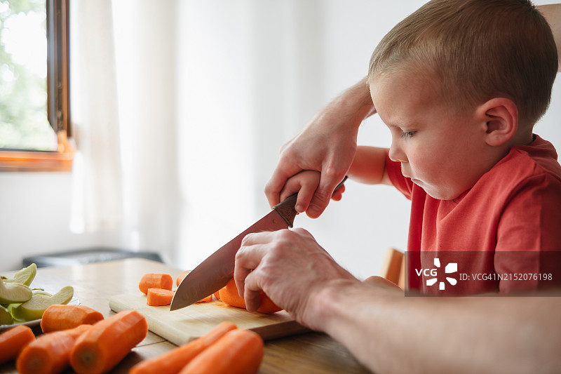 爸爸教他的孩子用刀切蔬菜。在厨房里帮助一个孩子。现代父亲图片素材