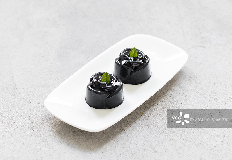 两个迷你玫瑰形状的黑色抹茶奶油蛋糕，在盘子上，浅灰色背景，特写图片素材