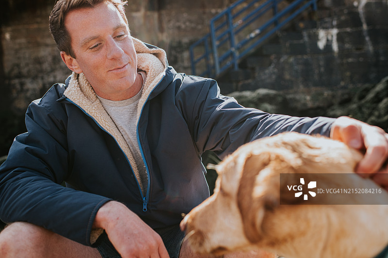 一位英俊的男人抚摸着他的金毛寻回犬图片素材