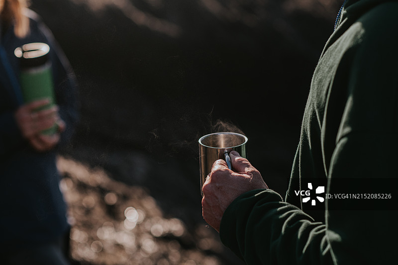 男人拿着不锈钢旅行杯，女人拿着保温瓶站在外面图片素材