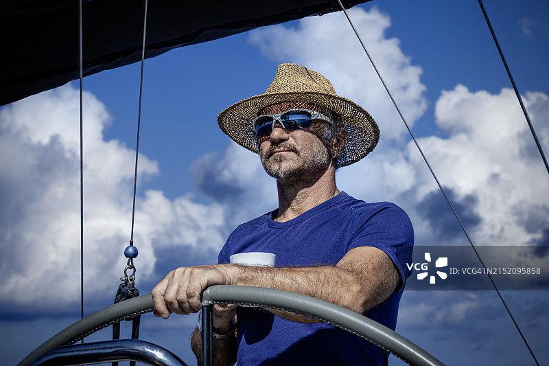戴着草帽的男人一边开帆船一边喝咖啡图片素材