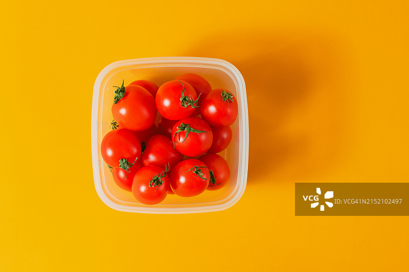 橙色背景上的塑料午餐盒里的红色樱桃番茄图片素材