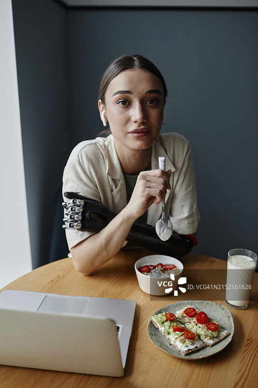 拥有仿生手臂的年轻女子在餐桌旁吃早餐图片素材
