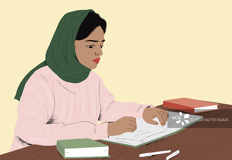 戴着头巾的女人在黄色背景的桌旁学习图片素材
