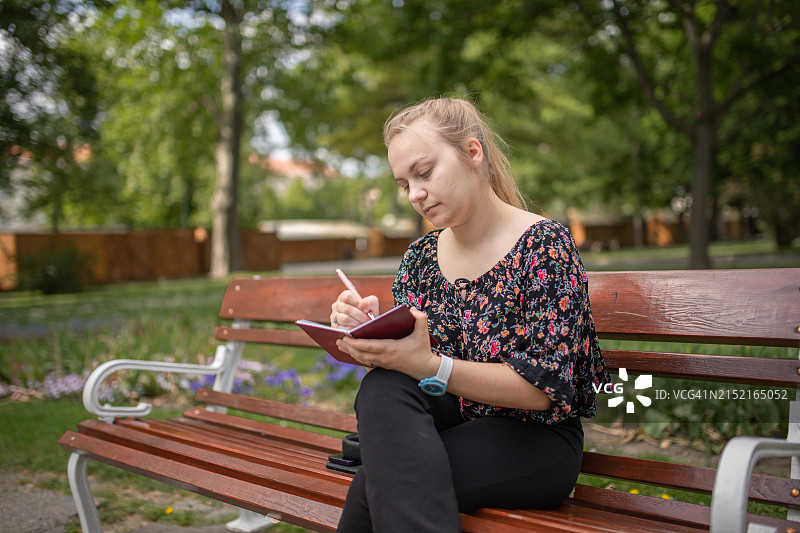 年轻女人坐在公园的长椅上写字图片素材