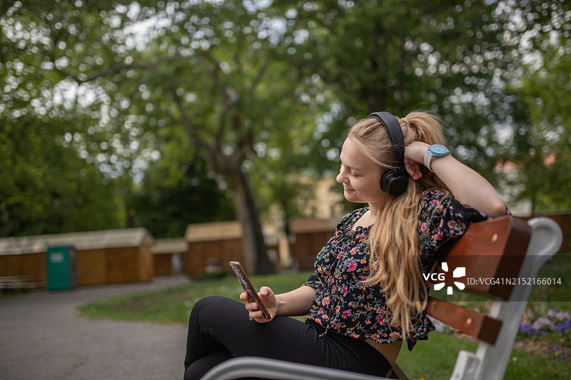 年轻的女大学生在休息时坐在公园里用耳机听音乐图片素材