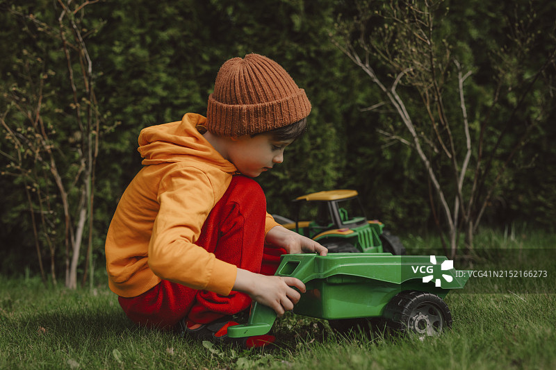 男孩在后院草地上玩绿色玩具拖拉机图片素材
