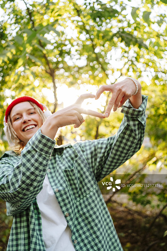 快乐的年轻女人在公园的树前比心图片素材