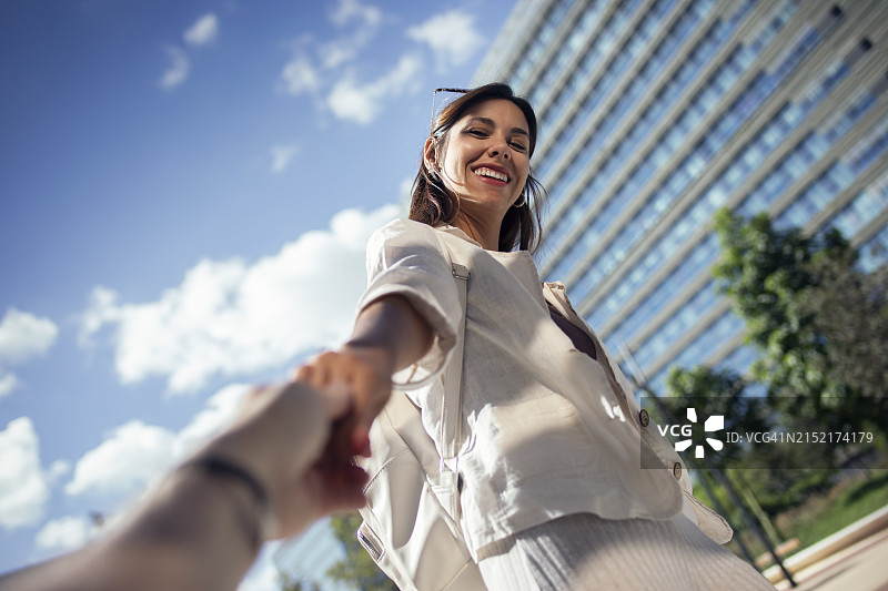 快乐的年轻女人牵着街上男人的手图片素材