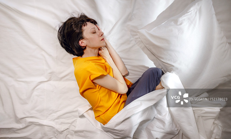 身穿黄色T恤，在家中床上枕着枕头睡觉的女人图片素材