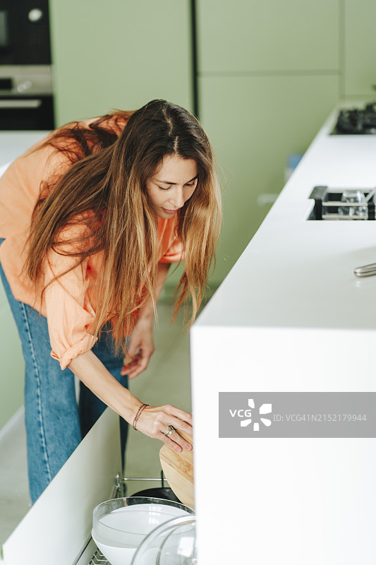 长发女人在家中将盘子放入洗碗机图片素材