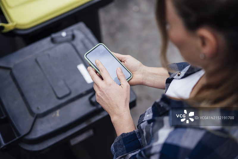 中年妇女在垃圾桶旁使用智能手机图片素材