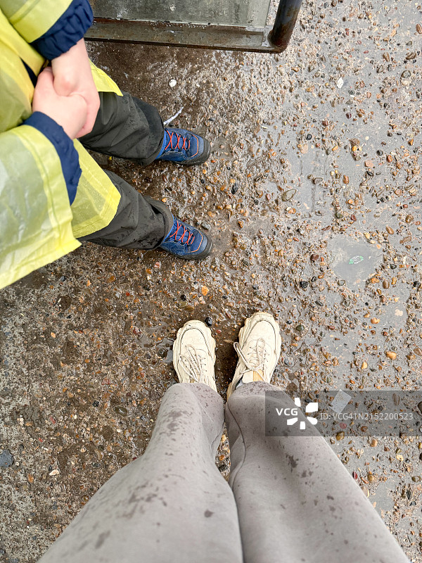 雨中湿沥青地上男孩的白色运动鞋和蓝色鞋子，俯视图图片素材