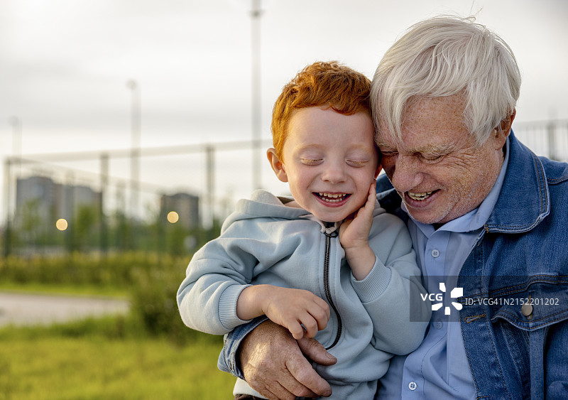 微笑的红发男孩和祖父在公园里图片素材