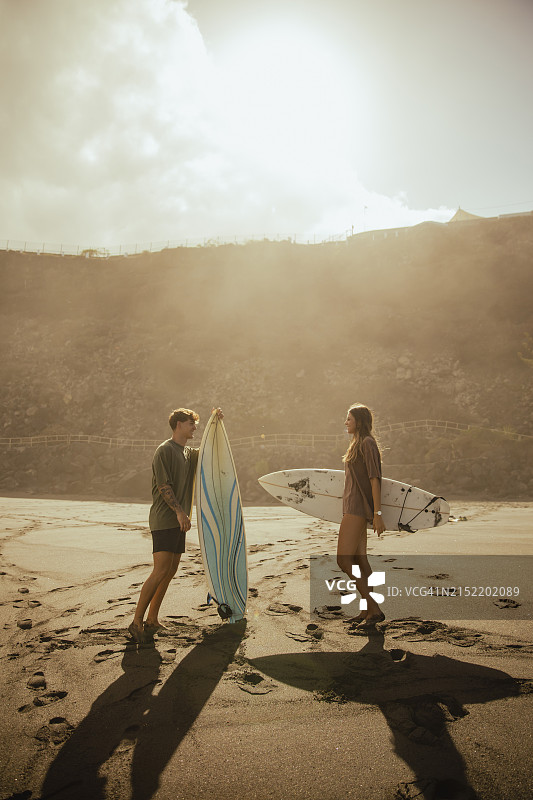情侣在阳光明媚的海滩上拿着冲浪板交谈图片素材