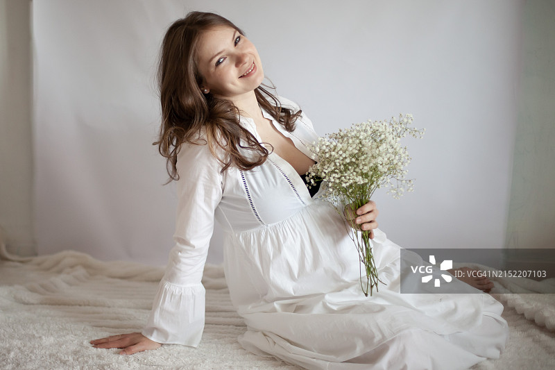 身穿白衬衫、手捧鲜花的孕妇（27-29周）图片素材