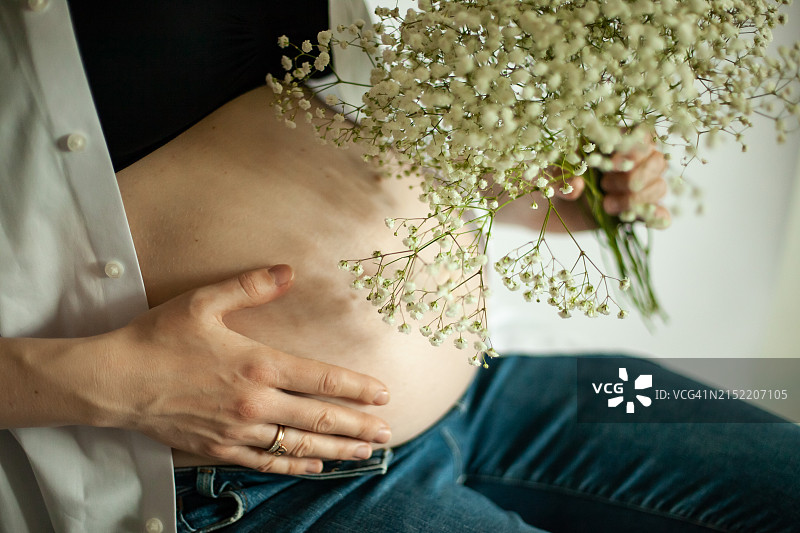 身穿白衬衫、手捧鲜花的孕妇（27-29周）图片素材